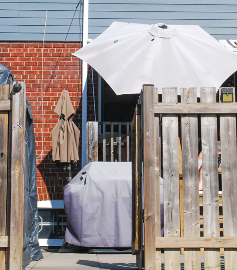 back of house, alley view, wood fence, white sun umbrella, grey cover on barbecue