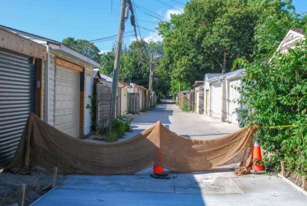 low burlap barrier draped across an alley, repairs being made to the concrete and pavement behind the barrier