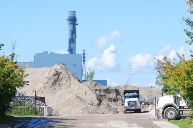 a dump truck parked beside a large pile of dirt, industrial site behind it 