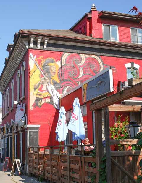 woman on patio of duke tavern, red building with mural on the side, white umbrellas,
