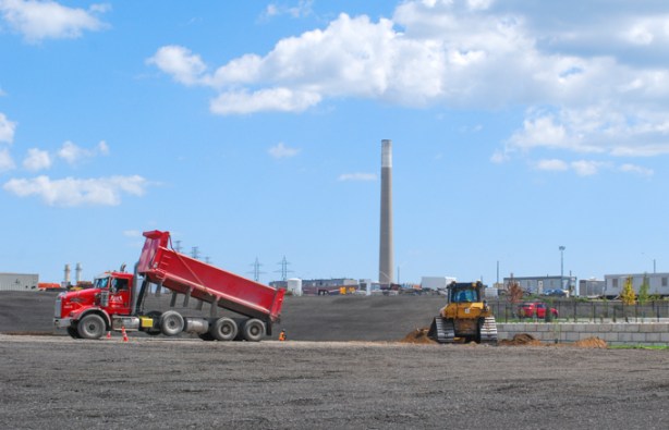 red dump truck releasing its load of dirt, adding to dirt on vacant lot in port lands
