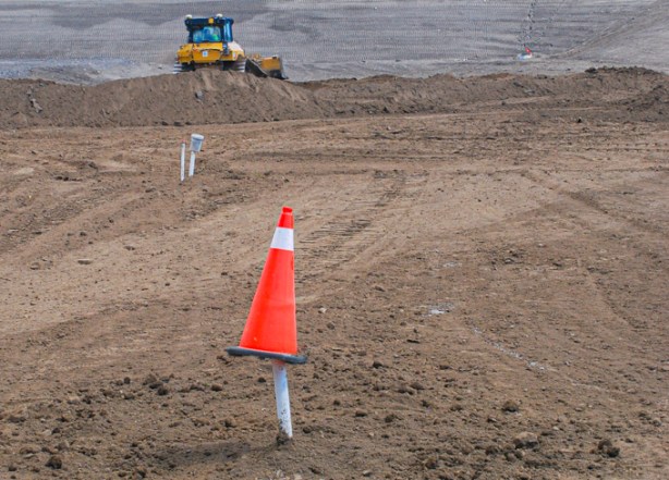 a small orange and white cone covers the top of a pipe coming up from underground, a bulldozer in the background, vacant land, just dirt