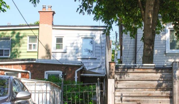 alley views, back of two semi detached houses, that share a chimney, one green siding and one one white siding