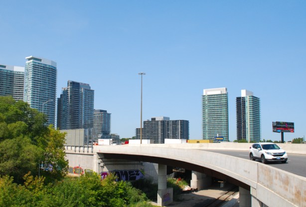 cars on ramp between eastbound 401 and Leslie Street, highrise glass and steel condos behind, GO train tracks under the ramp, view from pedestrian bridge over the tracks 