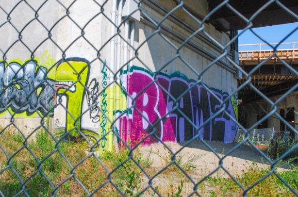 behind chainlink fence, graffiti on concrete pillars holding up the 401 highway