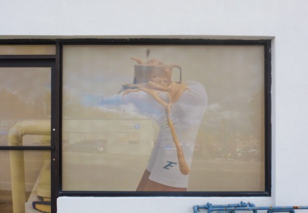 faded picture on exterior wall, overflowing cup of coffee or tea on bottom of foot that is upside down, wearing white sock