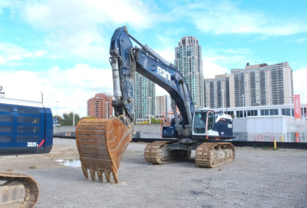 large digger on construction site, with glass and steel condos in the background