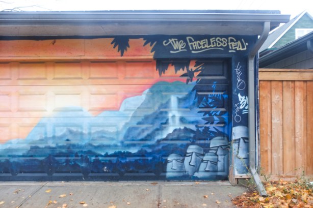 faceless few mural covers the front of a garage including both doors at number 15, in an alley, mural is in orange and blue