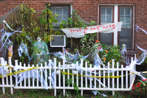 halloween decorations, including hand written sign that says enter if you dare, skeletons, fake cobwebs, yellow caution tape, all behind a little white picket fence