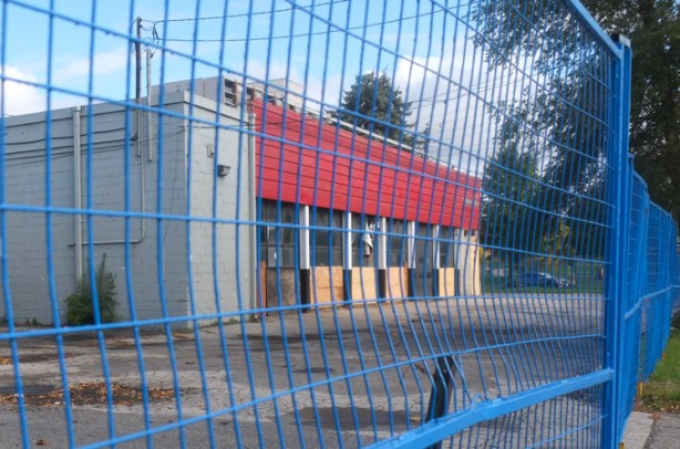 blue metal xonstruction fence in front of an empty building with parking lot in front of it