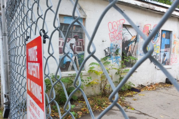 private property, no trespassing sign on chain link gate, in front of driveway, beside building with old pictures displayed in boarded up windows