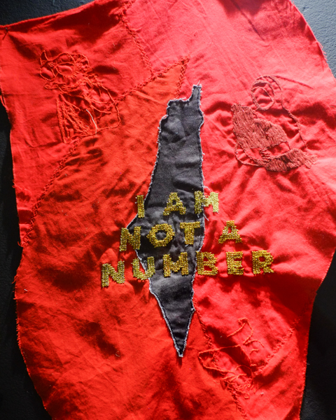 fabric art, mostly red with gold text embroidered that says I am not a number