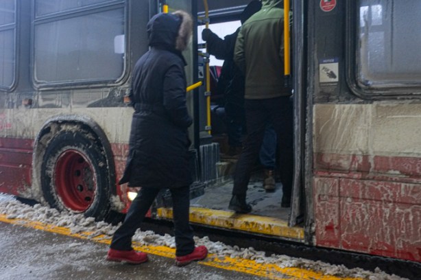 people entering the back door of a very dirty mud and slush covered bus