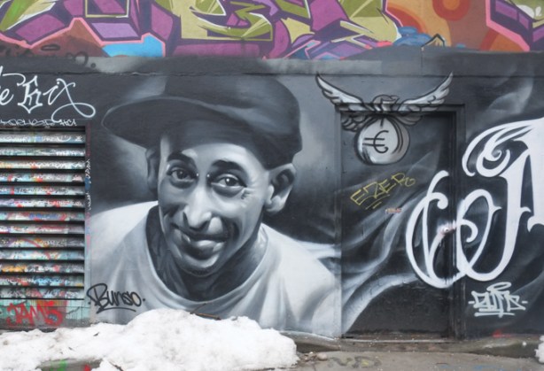 black and white portrait, street art mural, graffiti alley, man in white t shirt and black cap, smiling, 