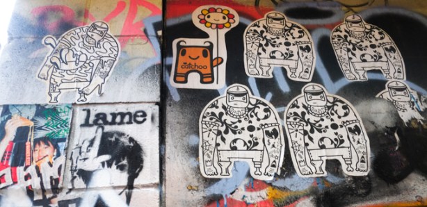 lots of paper pasteup graffiti in graffiti alley, one is a catchoo character holding a daisy shaped balloon