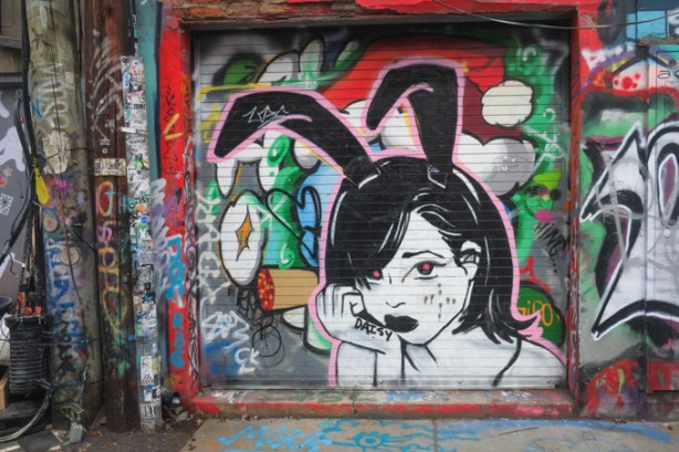 word daisy written on arm of girl in street art painting, graffiti alley, she has black rabbit ears