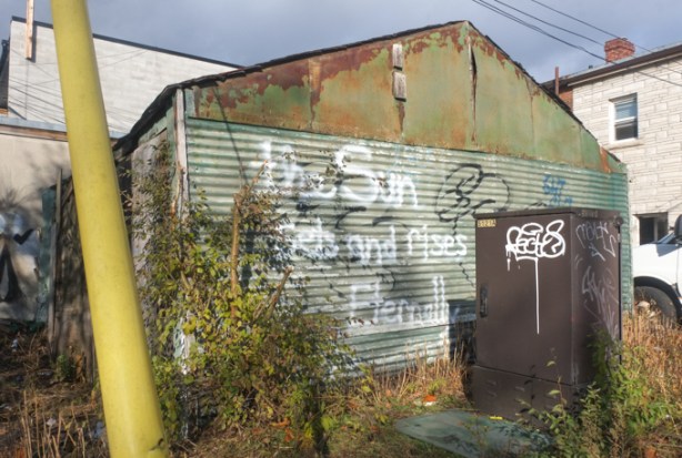 old garage with corrugated metal wall, graffiti on metal that says the sun sets and rises eternally