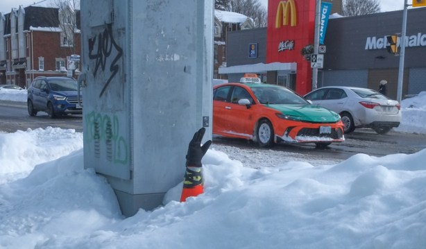 a black glove is on top of an orange cone in a snow bank, looks like an arm reaching up out of the snow