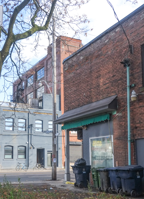 southwest corner of Glenlake and Dundas, old brick store with large window, looking across Dundas to older industrial or warehouse buildings, brick