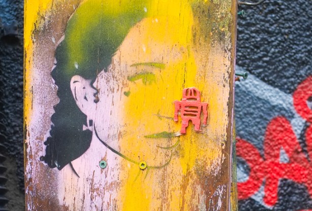 small red stikman on yellow paint with a woman's face at the bottom layer