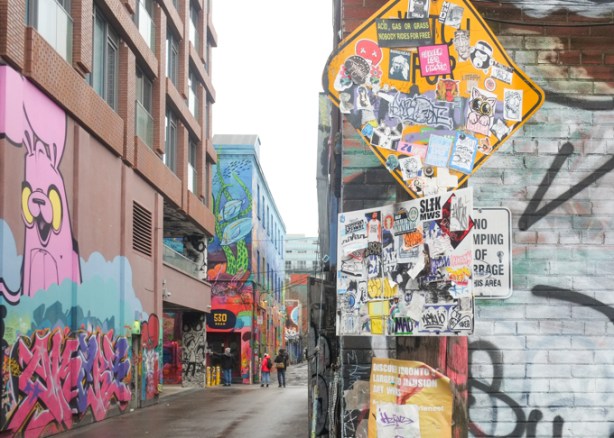 graffiti stickers covering signs at the entrance to graffiti alley where there is lots of street art in the background