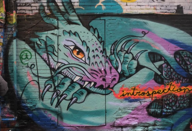 a street art painting of a greenish grey dragon with the word introspection in orange across its body