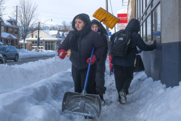 girls in winter outerwear, and carrying shovels, walking on snow covered widewalk