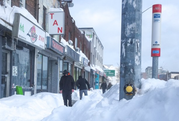 people walking on sidewalk, snow banks beside them