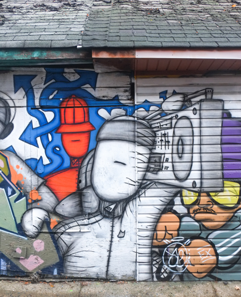 part of a street art mural on a garage in an alley, white man with ghetto blaster on his shoulder