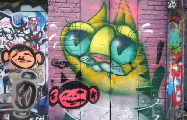 ugly cat, yellow, with bulging green eyes, street art mural, with two monkey faces, graffiti alley
