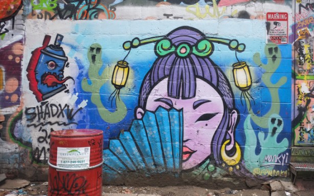 street art painting by Monk Yi, woman holding a blue fan, with her hair tied up and two little lanterns in her hair, big gold ear rings. 