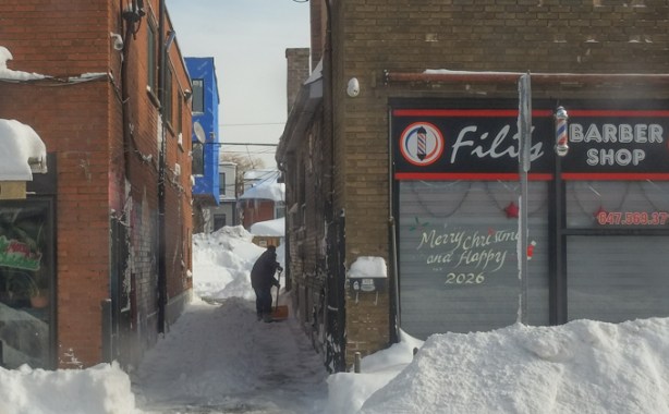 a man shovels a snowy alley, between two stores
