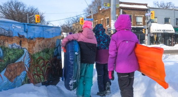 a group of kids with inner tubes and sleds, walk on sidewalk