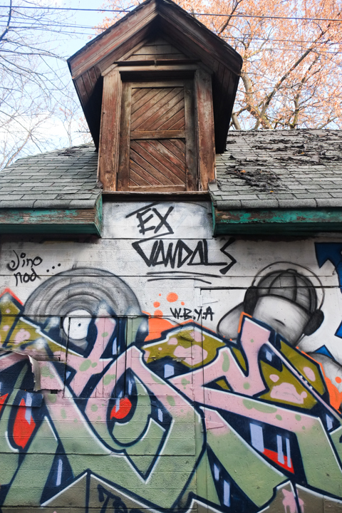 street art on the side of a garage in an alley, also a small window jutting out from roof, wood,