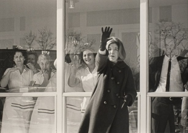 picture of a woman standing outside a window, inside there are other people looking out
