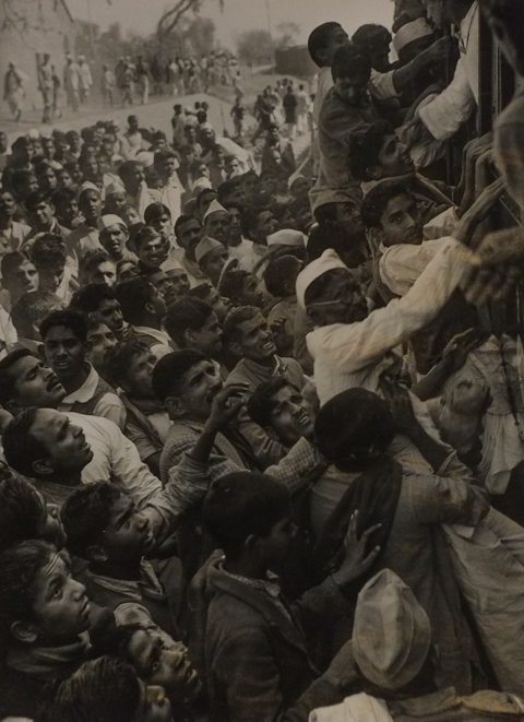 crowds in India following Mahatma Gandhi,, many are clinging to the side of a train, and many more are following along beside the train