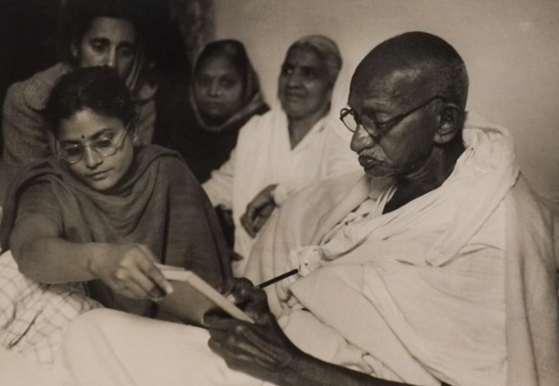 Henri Cartier-Bresson's 1947 photo of Mahatma Gandhi in India, sitting in a bed writing on a book that a woman is holding