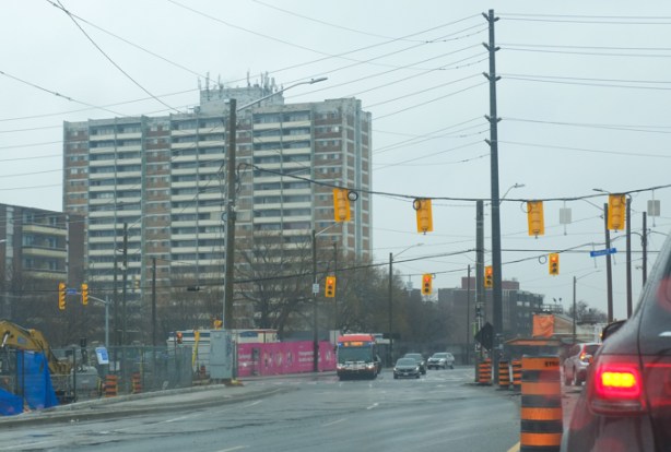looking northeast along eglinton ave at midland avenue, rainy day, apartment building on corner, bus, traffic
