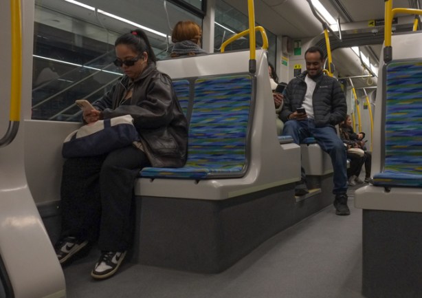 people sitting on an Eglinton LRT train, one is on her phone, 