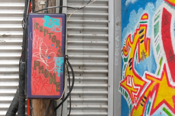 electrical box in alley painted red, with words painted on it, raptors phone