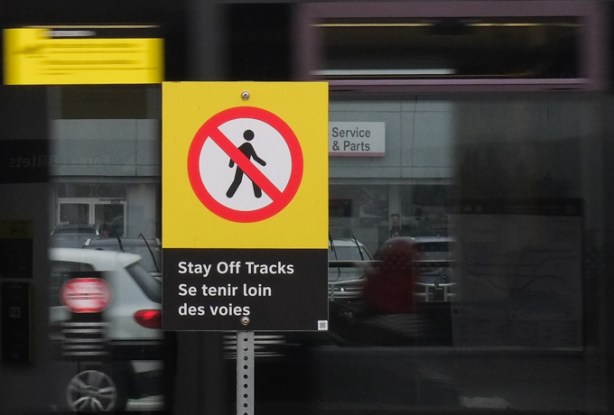 sin saying stay off tracks in english and in french, with a train passing behind the sign