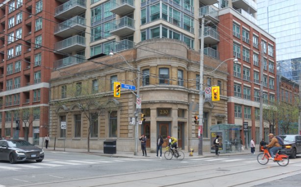 northeast corner of King and Sherbourne, number 230 King is old bank building, glass and steel condos rising behind it