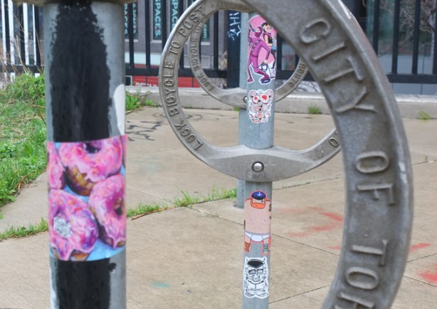 graffiti stickers on city of toronto bike parking rings, pink iced donuts, visual noise, 