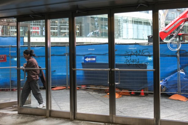 glass doors on Bloor street, entrance from subway to street, woman entering, blue hoardings outside because of construction on bloor street