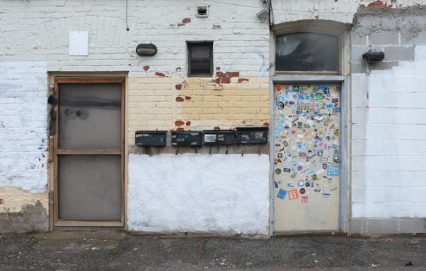 side entrances to a building, two doors with 4 mailboxes between them. one of the doors is covered with stickers