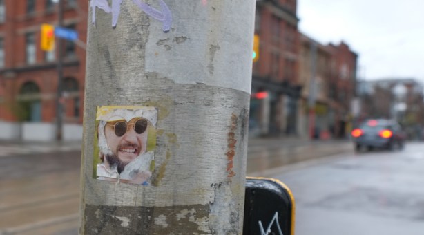 photo of a man's face, wearing sunglasses, pasteup graffiti on a pole