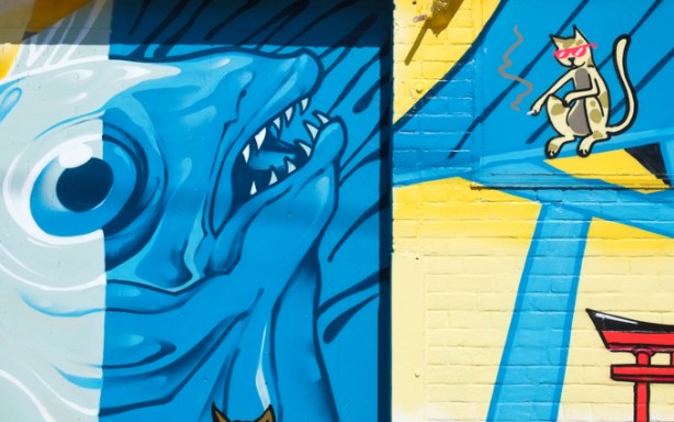 a portion of Japan Town 5 mural on the side of Sanko Trading Company store on Queen Street West, blue fish with large eye, open mouth with teeth, also a yellow cat and a red Japanese gate