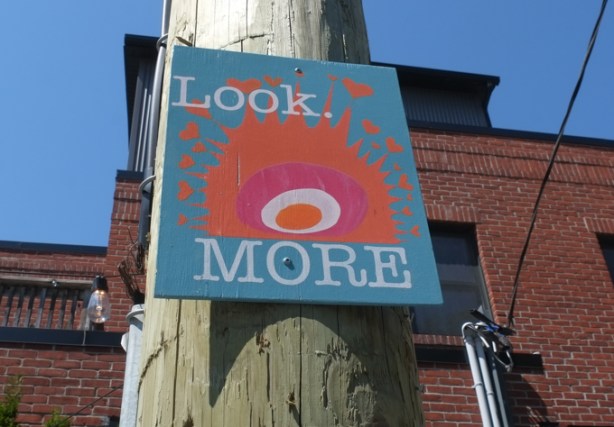 small painting nailed to a wood pole, with text that says look more