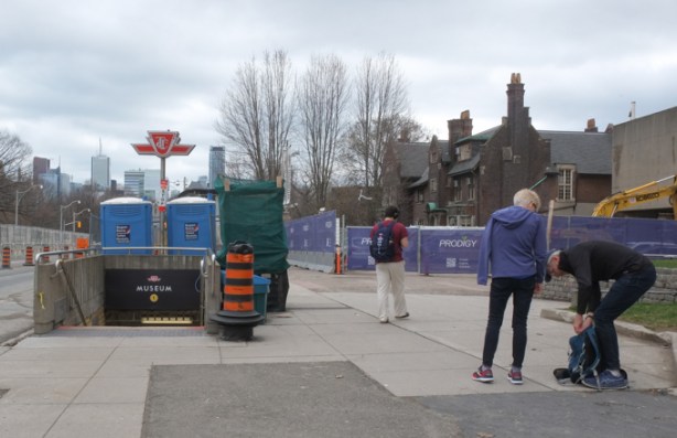 two people outside the museum near museum subway station entrance, that has two blue porta potties sitting beside it