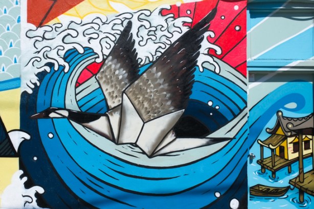 a portion of Japan Town 5 mural on the side of Sanko Trading Company store on Queen Street West, image of Canada goose, part in origami and part realistic, flying over a large blue wave